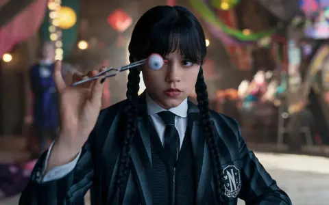 Wednesday Addams hält mit einer Pinzette ein künstliches Auge vor ihrem Gesicht. Ein Blick auf die kommende Staffel 2 von Wednesday.