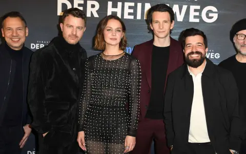 Das Ensemble des Films "Der heimweg" posiert lächelnd vor dem Banner.