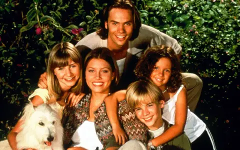 Die besetzung von eine himmlische familie: ein lächelnder Vater, drei Kinder und ein weißer Hund vor üppigem Grün.