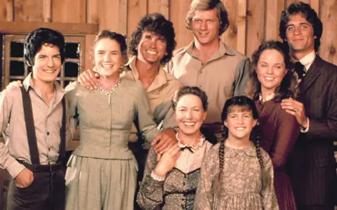 Die Besetzung von Unsere kleine Farm: Eine glückliche Familie posiert vor einer Holzwand.