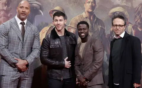 Die Besetzung von Jumanji: Dwayne Johnson, Nick Jonas, Kevin Hart und Jake Kasdan posieren vor einem Dschungel-Hintergrund.