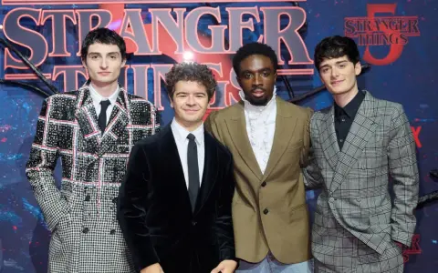Die Besetzung von Stranger Things posiert vor dem Logo der Serie.