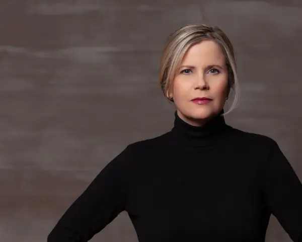 Porträt einer Frau mit blonden Haaren und einem schwarzen Rollkragenpullover. Sie könnte eine Schauspielerin sein, die in **Filme von Michaela Schaffrath** mitspielt.