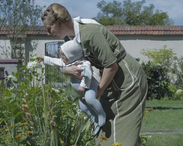 Frau mit Baby im Garten vor blühenden Blumen.