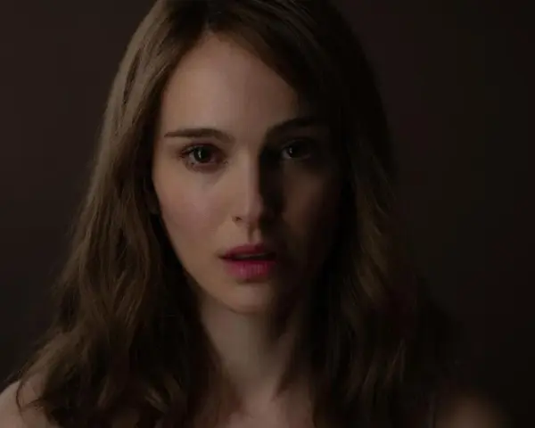 Natalie Portman, bekannt aus vielen Filmen, blickt nachdenklich in die Kamera. Ihr Gesicht ist im Schatten, nur ihre Augen und Lippen sind beleuchtet.