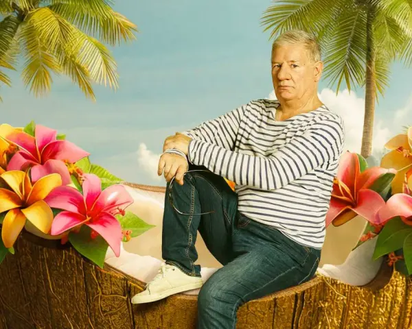 Ein Mann sitzt in einer Kokosnussschale, umgeben von tropischen Blumen und Palmen. Ein Bild, das an Filme von Claude-Oliver Rudolph erinnert.