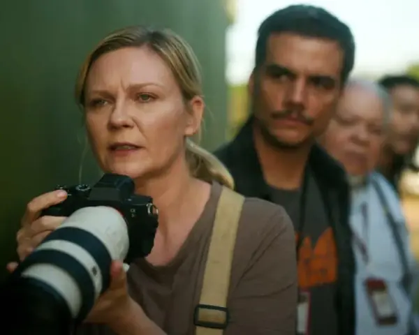 Kirsten Dunst mit Kamera, Teil der besetzung von Civil War, im Hintergrund unscharfe Personen.