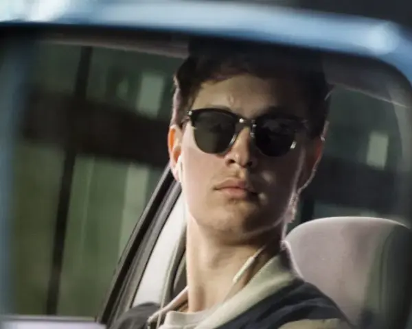 Ein junger Mann mit Sonnenbrille und Kopfhörern im Rückspiegel, der an die Besetzung von Baby Driver erinnert.