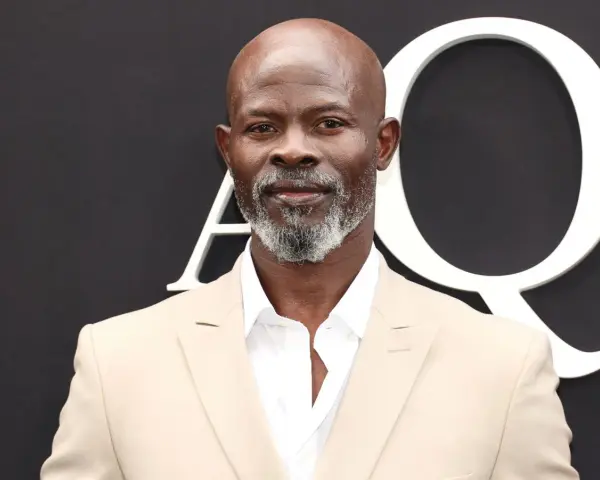 Djimon Hounsou, bekannt aus vielen Filmen, trägt einen hellbeigen Anzug und ein weißes Hemd.