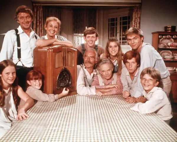 Die Besetzung von Die Waltons versammelt sich um ein Radio. Die Familie lächelt fröhlich in die Kamera.