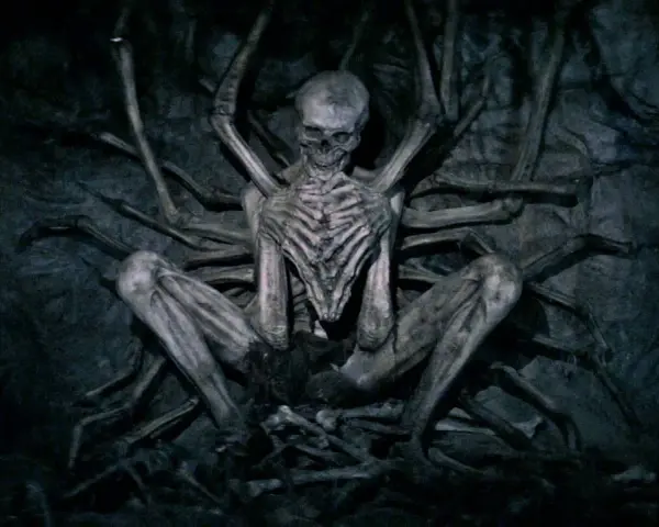 Ein skelettartiges Wesen, der leere Mann, sitzt in einer dunklen Höhle, umgeben von knochigen Gliedmaßen.