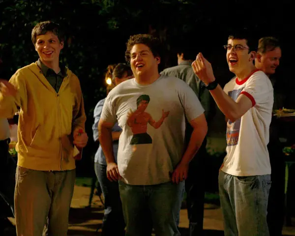 Die Besetzung von Superbad feiert eine Party. Michael Cera, Jonah Hill mit Bruce Lee T-Shirt und Christopher Mintz-Plasse lachen ausgelassen.