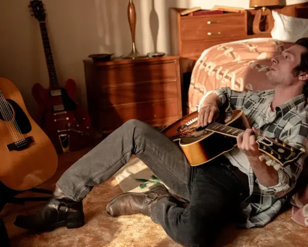 Ein Mann mit Gitarre, inspiriert von Bruce Springsteen, sitzt im Zimmer. Mehrere Gitarren stehen im Hintergrund.