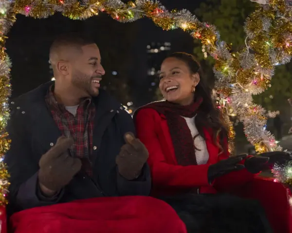 Ein glückliches Paar in einer Kutsche, geschmückt mit Lichterketten. Sie lachen und zeigen aufeinander. Vielleicht ein Versprechen: "Meet me next Christmas.