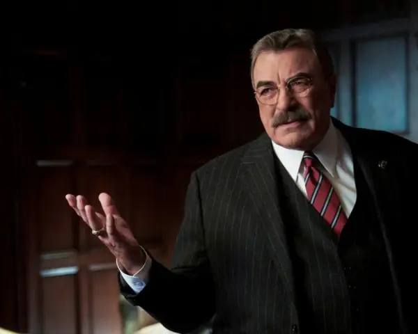 Frank Reagan in Blue Bloods Staffel 14, mit gestreiftem Anzug und Krawatte, erklärt etwas mit erhobener Hand.