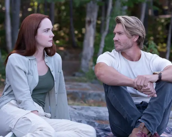 Ein Mann und eine Frau sitzen im Wald und schauen sich an. Sie sind Charaktere aus Sullivan's Crossing Staffel 4.