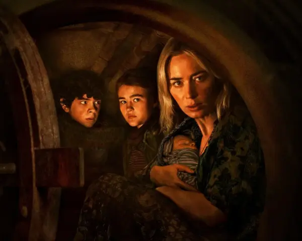 Die Besetzung von A Quiet Place: Eine Mutter hält ihr Baby, während ihre Kinder ängstlich in einem dunklen Versteck kauern.