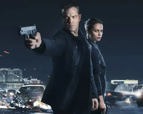 Jason Bourne und Alicia Vikander in Aktion. Ein Auto brennt, während Jason eine Waffe abfeuert. Die besetzung von Jason Bourne ist bereit für den Kampf.