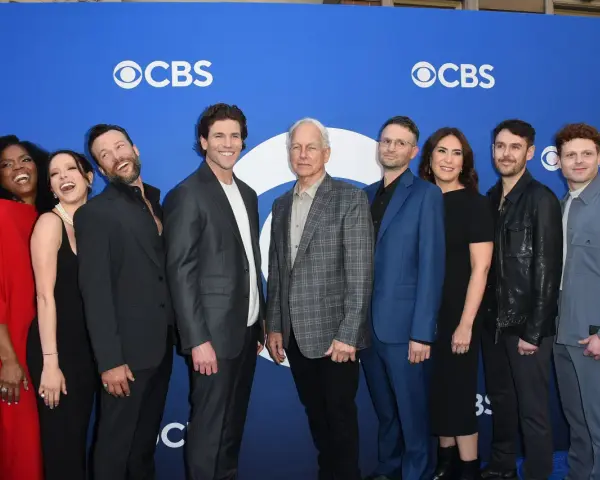 Die Besetzung von Navy CIS: Origins posiert auf einem blauen Teppich vor dem CBS-Logo.