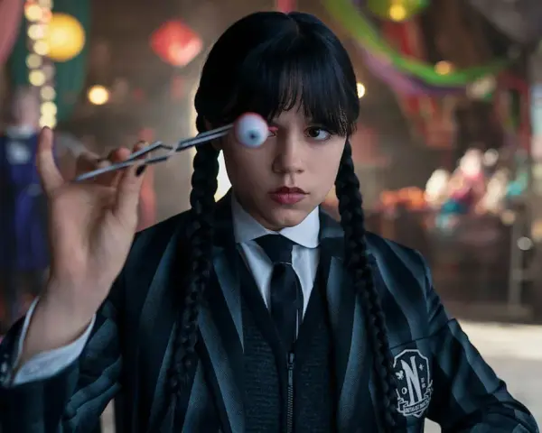 Wednesday Addams hält mit einer Pinzette ein künstliches Auge vor ihrem Gesicht. Ein Blick auf die kommende Staffel 2 von Wednesday.