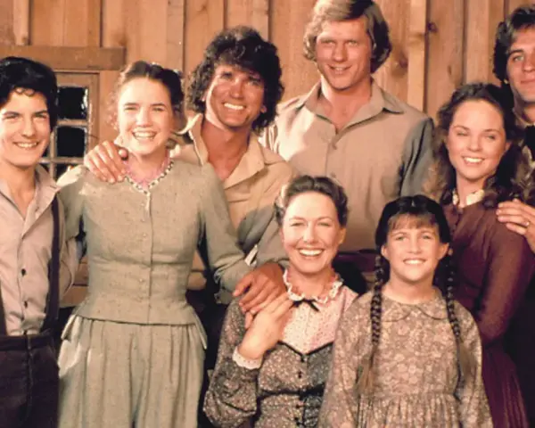 Die Besetzung von Unsere kleine Farm: Eine glückliche Familie posiert vor einer Holzwand.