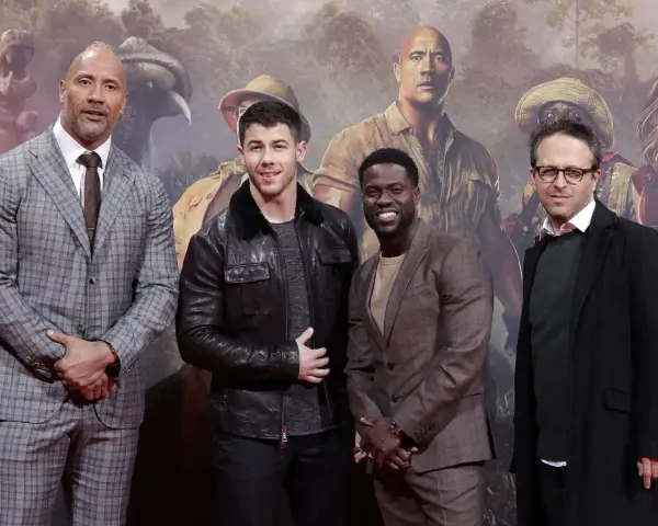 Die Besetzung von Jumanji: Dwayne Johnson, Nick Jonas, Kevin Hart und Jake Kasdan posieren vor einem Dschungel-Hintergrund.