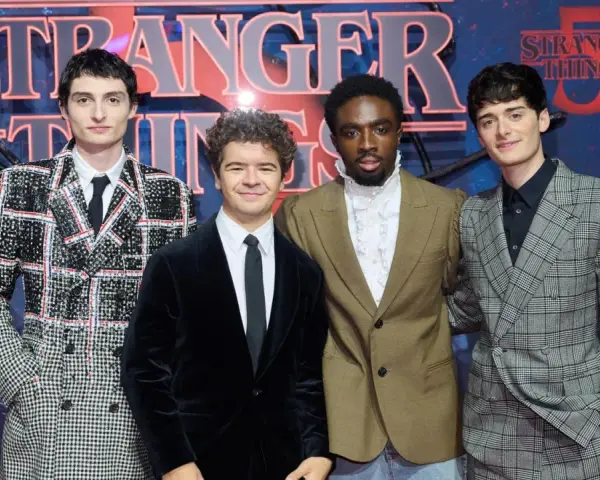 Die Besetzung von Stranger Things posiert vor dem Logo der Serie.