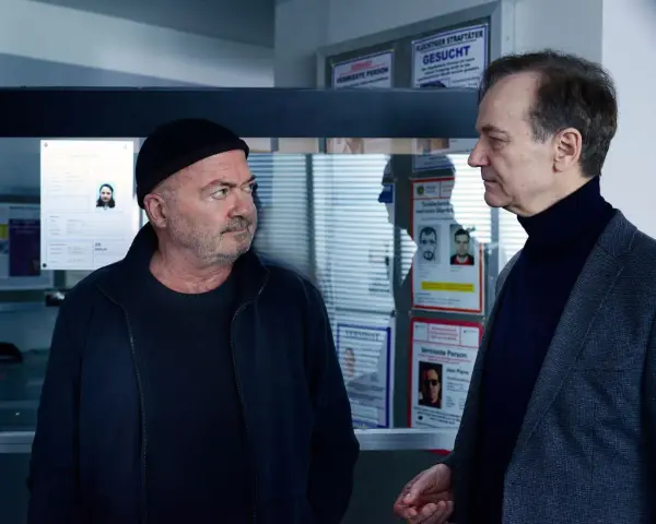 Zwei Männer, ein starkes Team, blicken auf Fahndungsplakate.