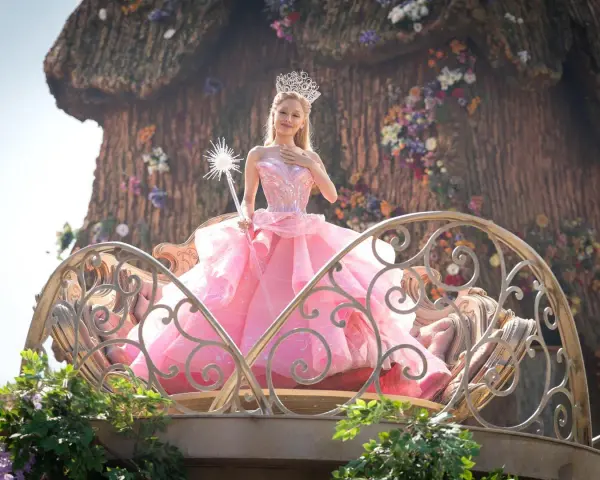 Ariana Grande als Glinda im Film "Wicked", in einem rosa Ballkleid und mit Zauberstab.