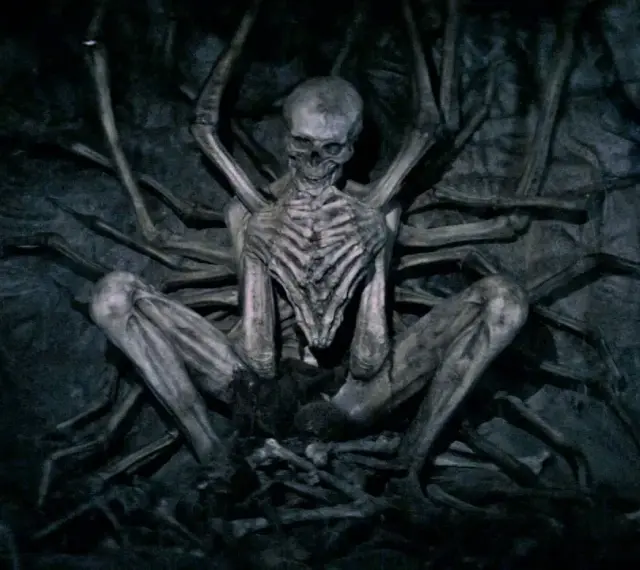Ein skelettartiges Wesen, der leere Mann, sitzt in einer dunklen Höhle, umgeben von knochigen Gliedmaßen.