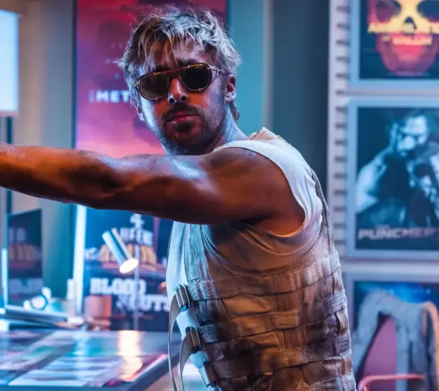 Ryan Gosling in Sonnenbrille, lehnt an einer Wand mit Postern seiner Filme.