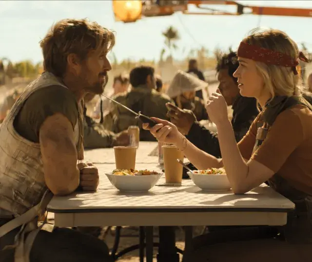 Ein Mann und eine Frau sitzen an einem Tisch, essen und unterhalten sich. Sie könnten die Hauptfiguren in "the fall guy" sein, die sich auf eine gefährliche Mission vorbereiten.