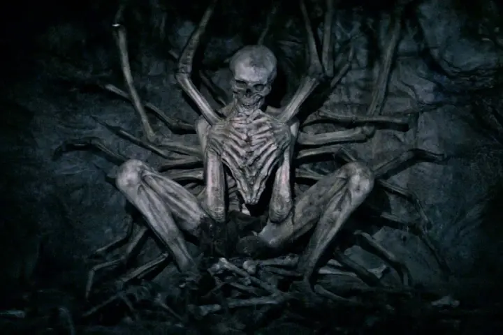Ein skelettartiges Wesen, der leere Mann, sitzt in einer dunklen Höhle, umgeben von knochigen Gliedmaßen.