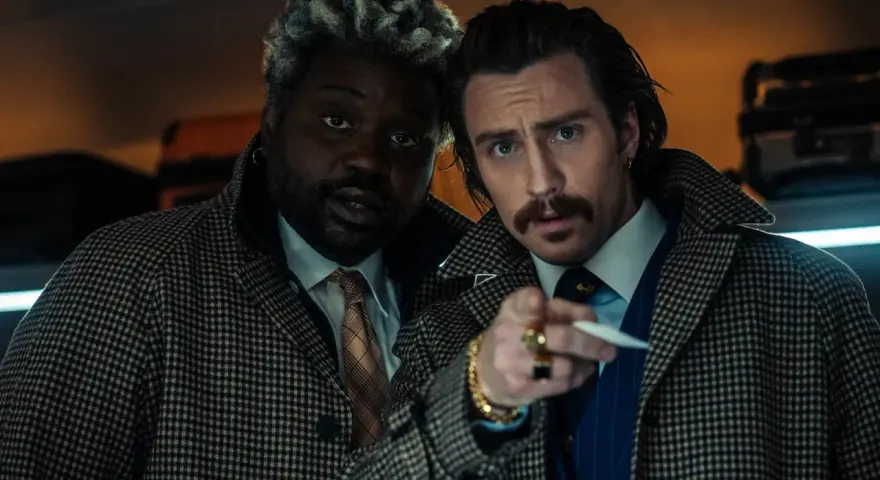 Aaron Taylor-Johnson und Brian Tyree Henry, Teil der Besetzung von Bullet Train, blicken ernst in die Kamera, während sie sich auf einem Zugabteil gegenüberstehen.