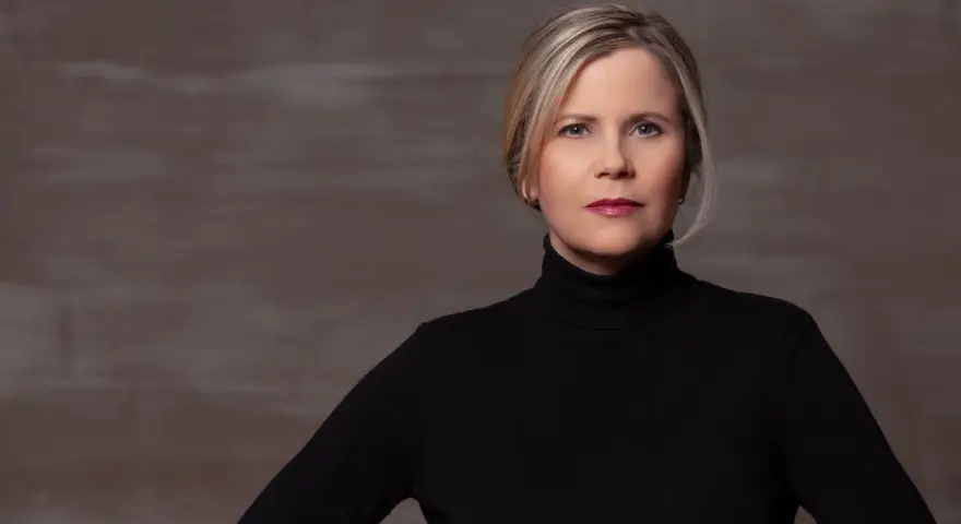 Porträt einer Frau mit blonden Haaren und einem schwarzen Rollkragenpullover. Sie könnte eine Schauspielerin sein, die in **Filme von Michaela Schaffrath** mitspielt.