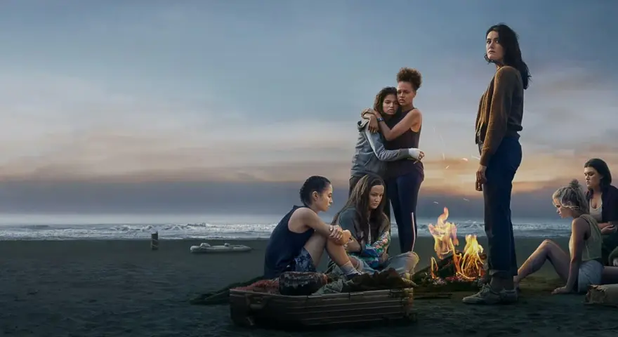Die Gruppe von Mädchen am Strand bei einem Lagerfeuer. Die Stimmung ist nachdenklich, wie in "The Wilds Staffel 3".