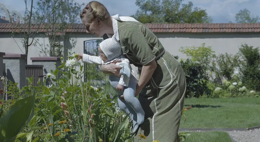 Frau mit Baby im Garten vor blühenden Blumen.