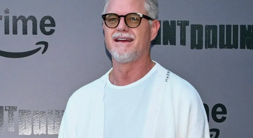 Eric Dane, bekannt für seine Rollen in Filmen und Serien, trägt eine Brille und ein weißes Outfit vor einem grauen Hintergrund mit dem Amazon Prime Logo.