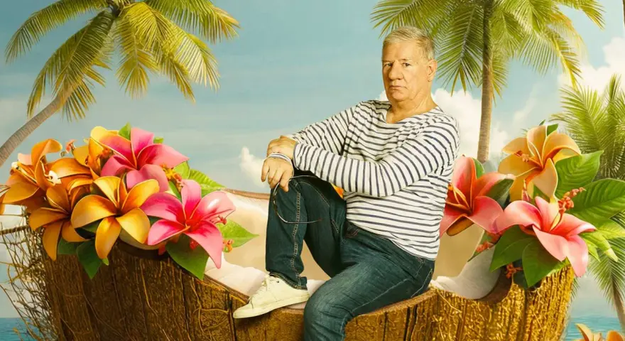 Ein Mann sitzt in einer Kokosnussschale, umgeben von tropischen Blumen und Palmen. Ein Bild, das an Filme von Claude-Oliver Rudolph erinnert.