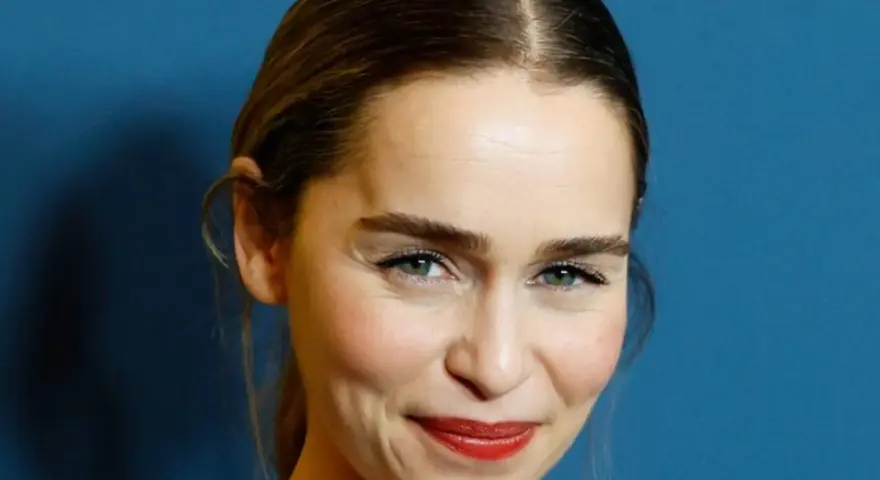 Emilia Clarke, bekannt für ihre Rollen in **filme und serien von Emilia Clarke**, lächelt charmant vor blauem Hintergrund.