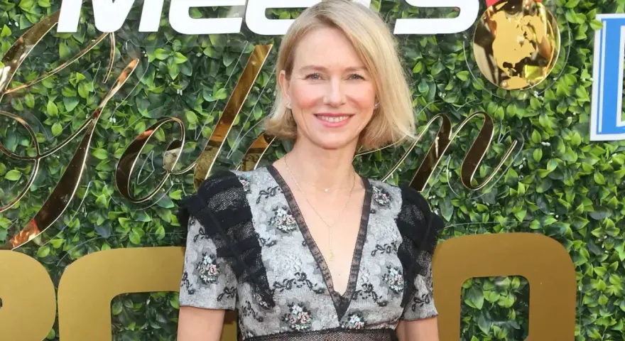 Naomi Watts lächelt vor einer grünen Wand mit goldenen Buchstaben. Sie trägt ein Kleid mit Blumenmuster. Ihre Filme sind oft spannend.