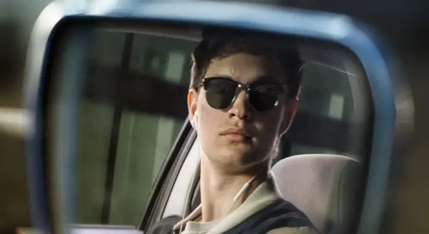 Ein junger Mann mit Sonnenbrille und Kopfhörern im Rückspiegel, der an die Besetzung von Baby Driver erinnert.