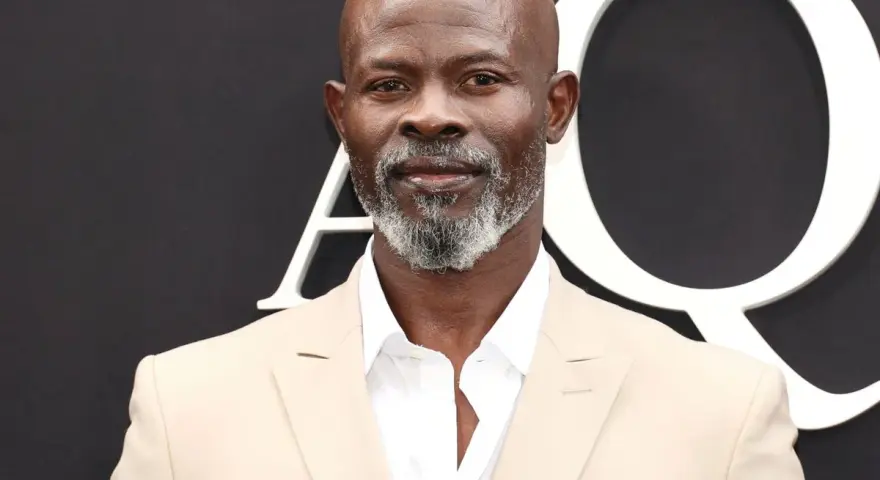 Djimon Hounsou, bekannt aus vielen Filmen, trägt einen hellbeigen Anzug und ein weißes Hemd.