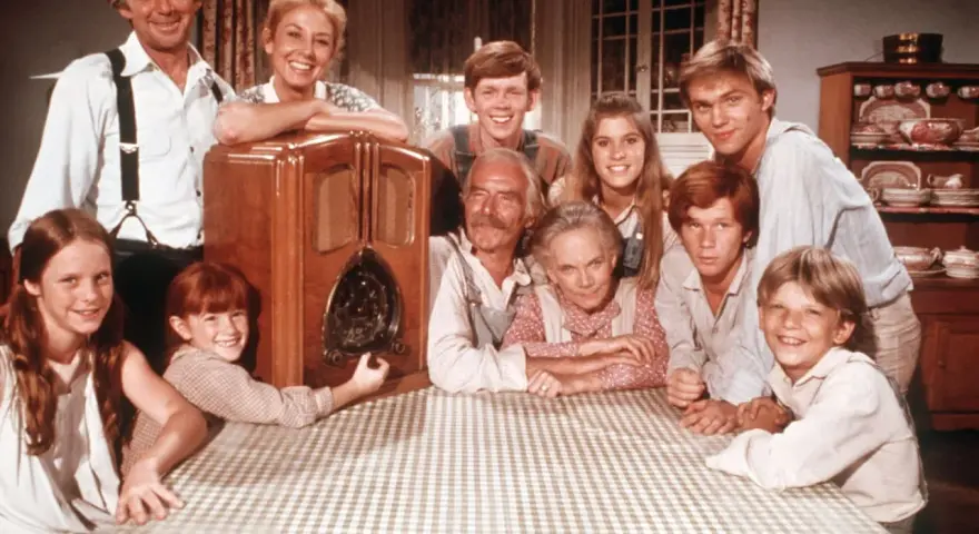 Die Besetzung von Die Waltons versammelt sich um ein Radio. Die Familie lächelt fröhlich in die Kamera.