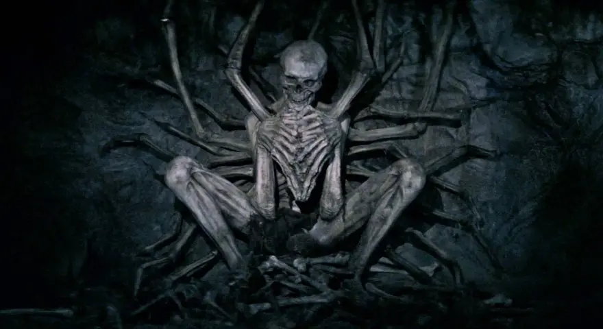 Ein skelettartiges Wesen, der leere Mann, sitzt in einer dunklen Höhle, umgeben von knochigen Gliedmaßen.
