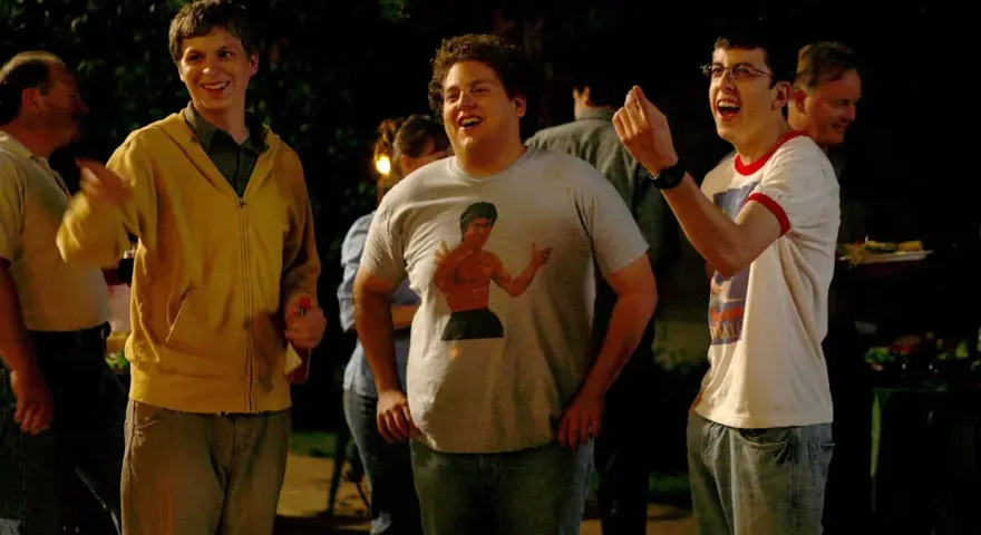 Die Besetzung von Superbad feiert eine Party. Michael Cera, Jonah Hill mit Bruce Lee T-Shirt und Christopher Mintz-Plasse lachen ausgelassen.