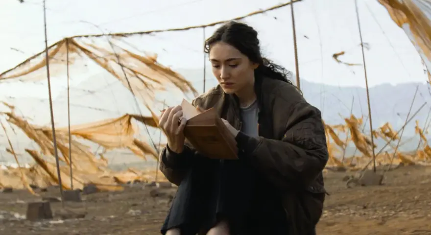 Eine junge Frau liest in einem alten Buch, umgeben von verwitterten Netzen. Ein Moment der Ruhe in der Welt von Oderbruch Staffel 3.