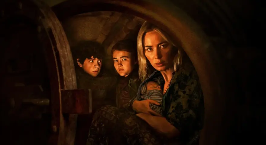 Die Besetzung von A Quiet Place: Eine Mutter hält ihr Baby, während ihre Kinder ängstlich in einem dunklen Versteck kauern.