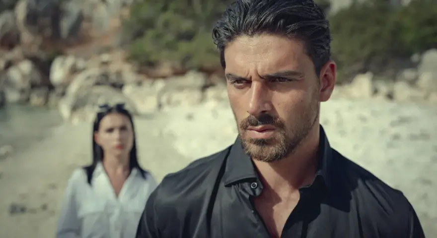 Michele Morrone, bekannt aus Filmen wie "365 Days", blickt nachdenklich in die Ferne, während eine Frau im Hintergrund steht.