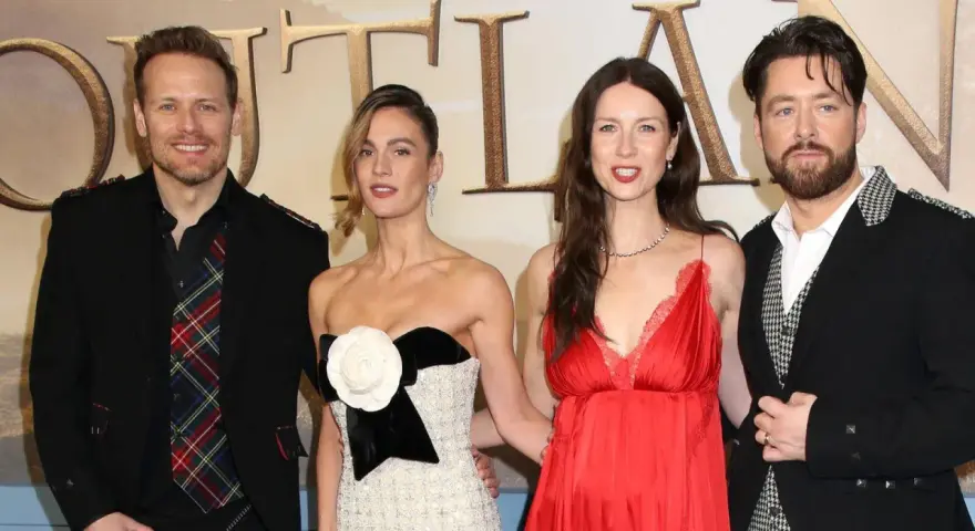 Die Besetzung von Outlander: Sam Heughan, Caitriona Balfe und Richard Rankin posieren lächelnd.